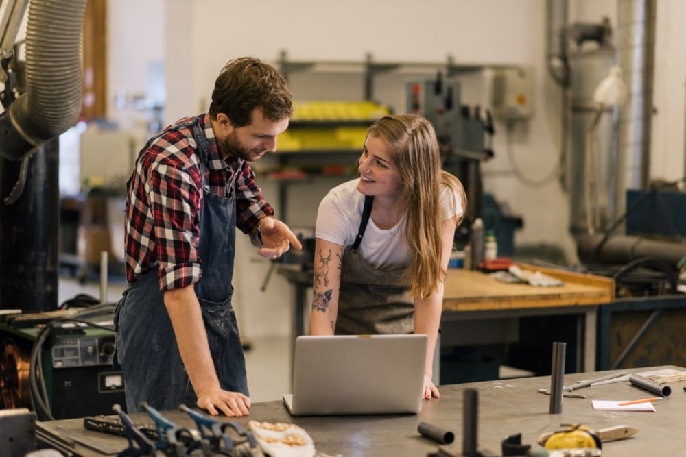 To ansatte i et verksted står og ser på en PC