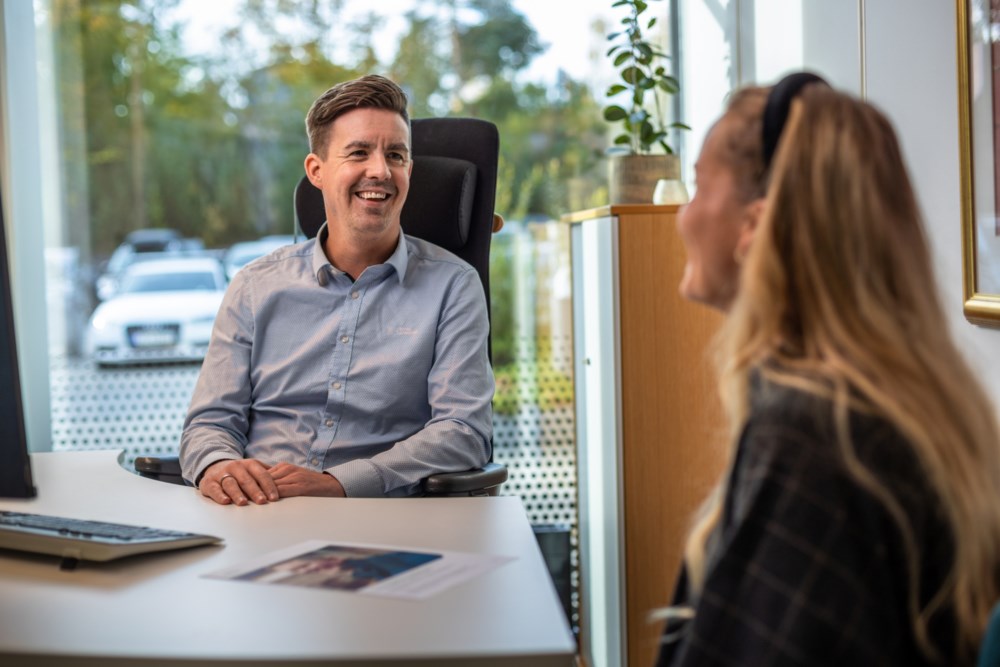 Rådgiverprat i banklokale med smilende rådgiver og kvinne